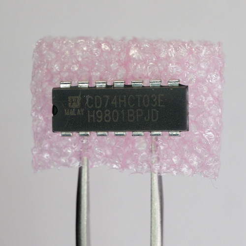 Top view of Harris CD74HCT03E integrated circuit held in tweezers against pink foam.