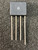 Flat-pack 4-pin bridge rectifier body, matte black plastic, circular center marking, four straight tinned leads, light surface scuff on face.