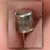 TO-18 metal can transistor held between fingers, marking partly hidden, gold-colored leads