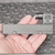 Gray rectangular body with right-angle black connector housing marked mPm; two mounting clips with visible pins; no wear or damage observed.