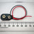 Top view of a 9V battery snap connector with coiled red and black leads alongside a millimeter ruler.