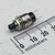 Perspective view of a C&K 8551MZQE2 subminiature pushbutton switch with mounting hardware beside a millimeter ruler.