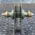 Olive-painted 6-plate stack with black center puck, dual threaded studs, brass hardware, and formed mounting feet. Light dust visible; no damage.