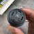 Face of the black Floyd Bell audible alarm held in hand, spoked grille, controller behind