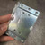 Hand holding zinc-plated mounting plate inside a clear poly bag