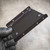 Gloved hand holding Crucial SSD bracket underside, folded side rails and dimpled screw holes visible