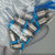 Sealed polybag containing 10 unused stainless-bodied fittings with blue thread protectors; hand-labeled "NR-20" visible; threads and bores uncontaminated.
