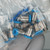 Sealed polybag labeled "NR-20" contains 10 stainless-bodied fittings with blue plastic thread-protection caps intact, threads clean and undamaged.