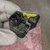 Black crinkle-finish body with PTT button, internal spring clip, and small lens port visible; light surface dust; yellow label partially visible in background.