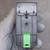 Dark gray plastic DIN-rail module, rear face shown. Green latch tab at lower center. Small circular numbered label upper-left corner. Single center screw visible.