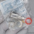 Silver-toned cylindrical connector body with gold-tipped center pin and two flat metal washers included; red circular label partially legible on bag.