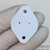 White mica or polymer TO-3 insulating pad with three mounting holes; matte flat finish, no markings; minor surface smudging visible.