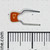 Orange ceramic disc body with partially legible markings; two radial leads bent horizontally outward. Leads appear uncut and undamaged.
