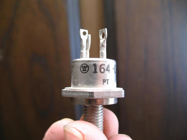 Closeup of a silvercolored Westinghouse 16409 power transistor, featuring a screwmount threaded stud base and two flat spade terminals for connections. The sturdy metal housing is marked with the iconic Westinghouse 'W' logo and the partial model number '1640' along with 'PT'. This 90V 20 Amp highpower semiconductor device is an industrialgrade studmount transistor, ideal for heavyduty electronic applications.