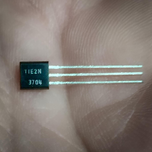 Texas Instruments 2N3704 transistor with plastic case and three through-hole leads held in a human hand.