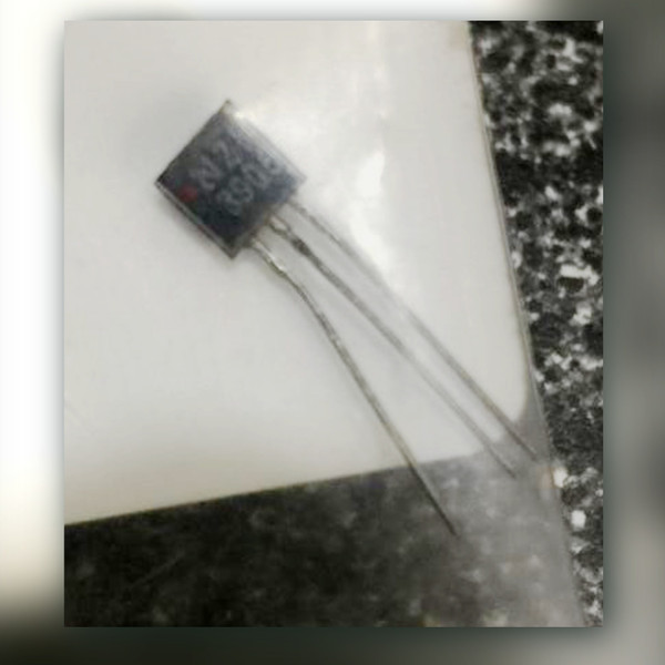 Black three-lead TO-92 transistor with a red dot on its face, resting on white backing