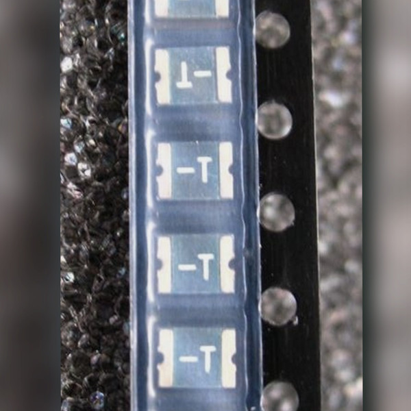 Carrier tape strip of resettable fuse chips marked -T on a dark speckled surface