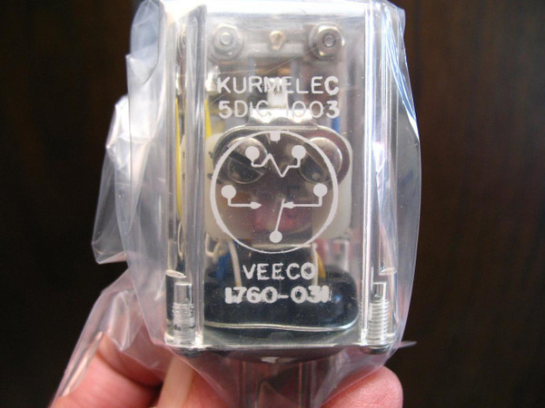 A close-up view of a VEECO 1760-31 electromagnetic time delay relay, encased in transparent plastic with metallic components inside. The label reads "KURT ELEC 5DIC-003 VEECO 1760-31." The relay is packaged in a plastic wrap and is available from PartsMine.com.