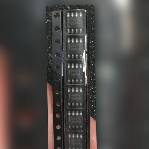 Row of seven eight-lead SOIC chips held between fingers over a dark speckled surface
