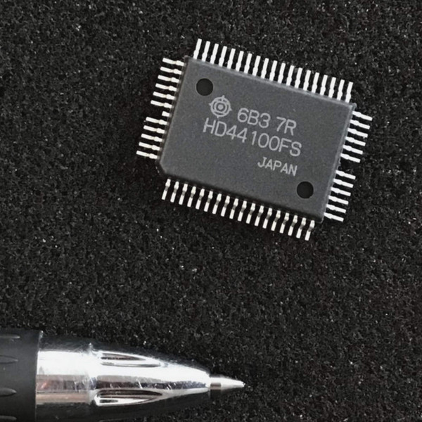 Hitachi HD44100FS 60-pin QFP LCD driver chip on a dark textured surface beside a pen tip