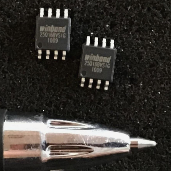 Two Winbond SOIC-8 flash chips marked 25Q16BVSIG on a dark textured surface beside a pen tip