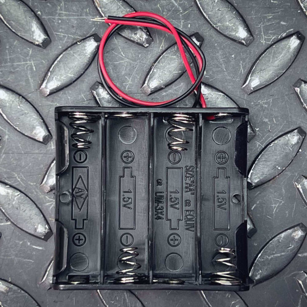 Black plastic 4-cell holder molded with SIZE AA or EQUIV and UM-3X4 markings, 1.5V per cell indicated, red and black wire leads attached.