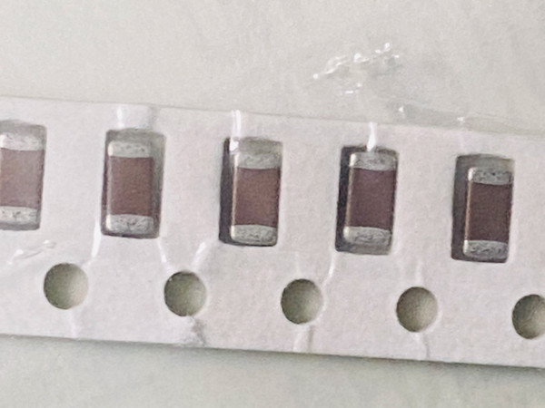 Five brown ceramic chip capacitors in paper tape with sprocket holes along bottom edge