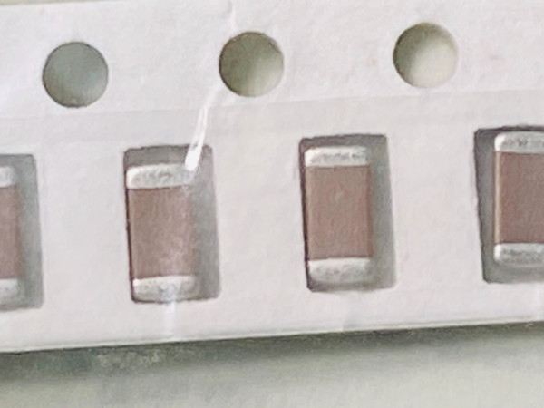 Macro of brown chip capacitors in paper tape, bag film creased across one pocket