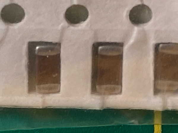 Three amber brown chip capacitors in tape, slightly soft focus, green mat below