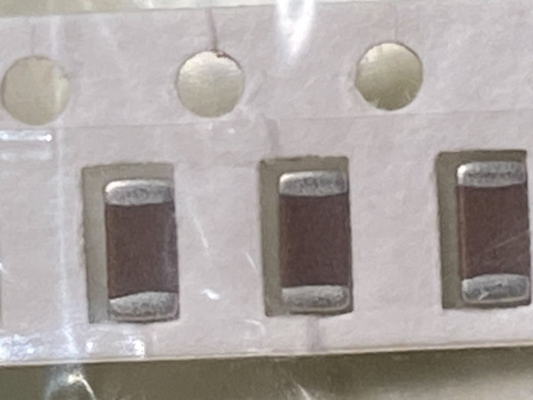 Close macro of three dark maroon chip capacitors seated in white paper carrier tape pockets