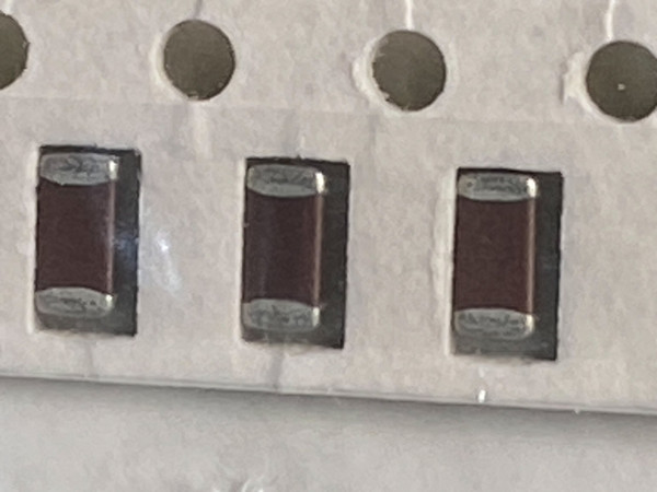 Macro of three brown ceramic chip capacitors in white tape pockets, sprocket holes above