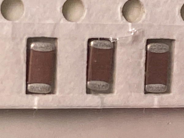 Macro of three brown chip capacitors seated in white carrier tape, holes above
