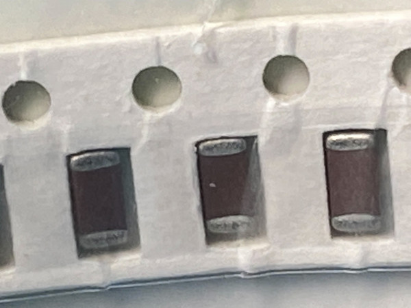 Tilted tape with three dark maroon chip capacitors and large sprocket holes above