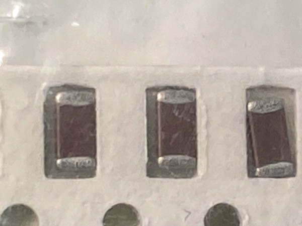 Close macro of three brown Panasonic chip capacitors seated in white carrier tape pockets