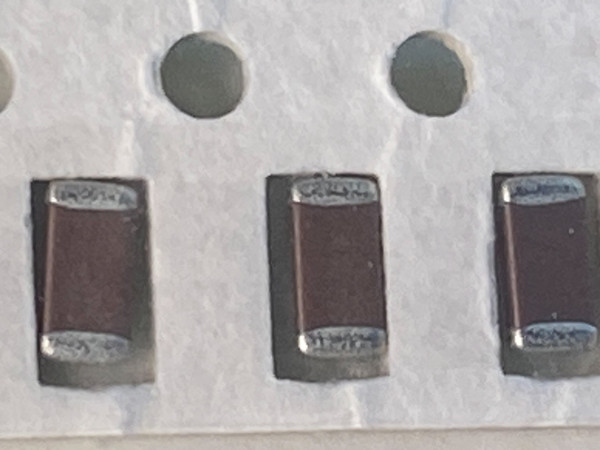 Macro of three dark maroon chip capacitors in tape, cut paper edge along bottom
