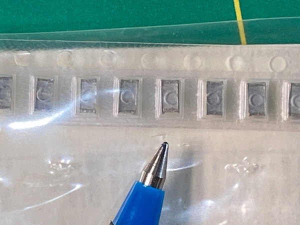Eight small gray SMD film capacitors held in clear carrier tape on white backing