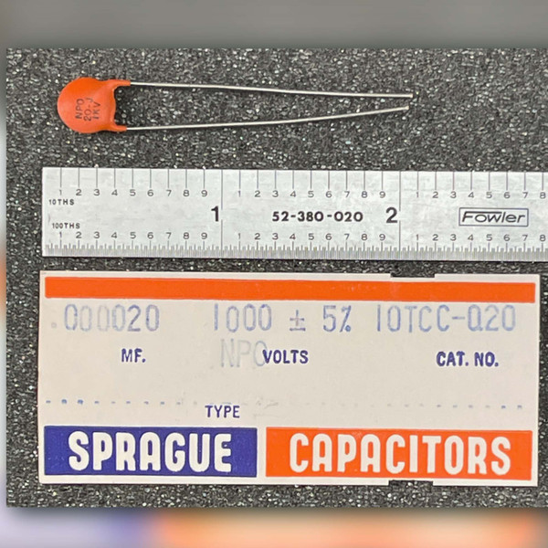 Small orange Sprague disc capacitor beside steel rule and carton label marked 10TCC-Q20