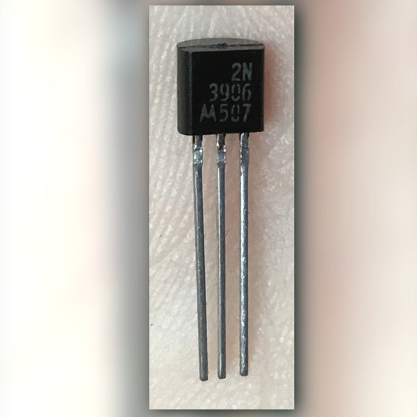 Black TO-92 marked 2N 3906 with batwing and 507, three straight leads, dark backdrop