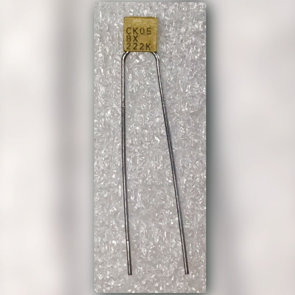 CK05BX222K 2200 pF ceramic capacitor, marking side up, splayed radial leads on light background