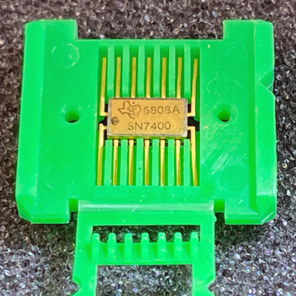 Gold ceramic flat-pack body marked SN7400 and date code 6808A, gold-plated leads appear straight and undamaged.