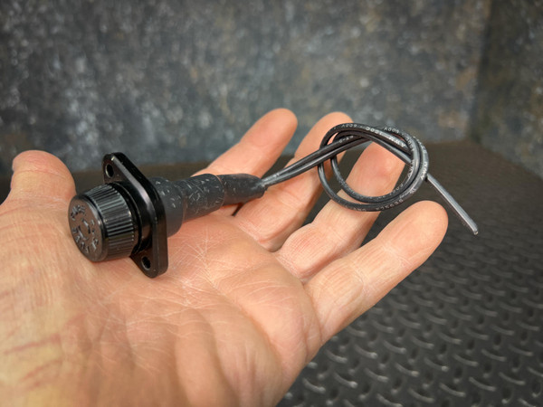 Black midget panel-mount fuse holder assembly with a knurled cap, a rectangular mounting flange, and two pre-attached black electrical leads, held in a person's open palm.