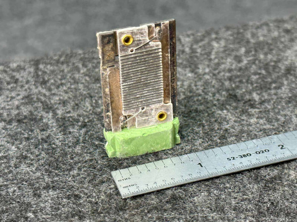 General Electric H0.55A Thermal Overload Heater Element, GE, a compact industrial electrical component. The heater element features a rectangular metallic body with a finely ridged surface for heat dissipation and two prominent goldcolored terminal holes at the top. Its base is encased in a bright green protective material. Shown on a textured gray background alongside a metal ruler for scale, this replacement part measures approximately 1.5 to 2 inches tall, ideal for motor starter, contactor, and circuit protection applications.