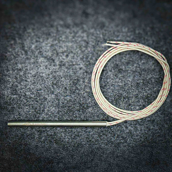 Stainless cartridge heater beside its coiled braided leads on a dark gray bench.