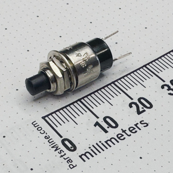 Perspective view of a C&K 8551MZQE2 subminiature pushbutton switch with mounting hardware beside a millimeter ruler.