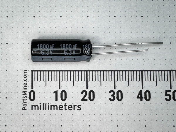 Black sleeved radial capacitor beside a millimetre ruler, sleeve printed 1800 uF 6.3V twice