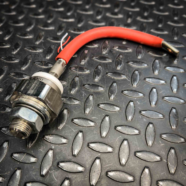 Stud-mount SCR body with threaded stud and hex nut, red wire lead with stripped end and ring terminal. Minor surface marks visible.