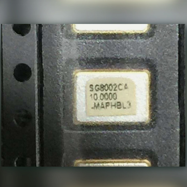Carrier-taped SMD oscillator labeled SG8002CA, 10.0000, MAPHBL3, neighboring parts partly in frame