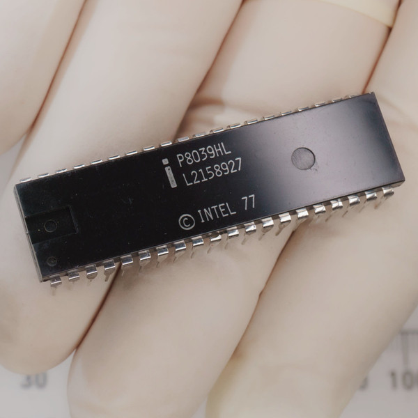 Gloved hand holds black 40-pin DIP marked P8039HL, L2158927, copyright INTEL 77.