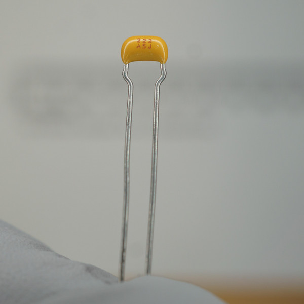 Yellow epoxy body marked "222 / ASJ"; both straight radial leads intact, no oxidation or bending visible.