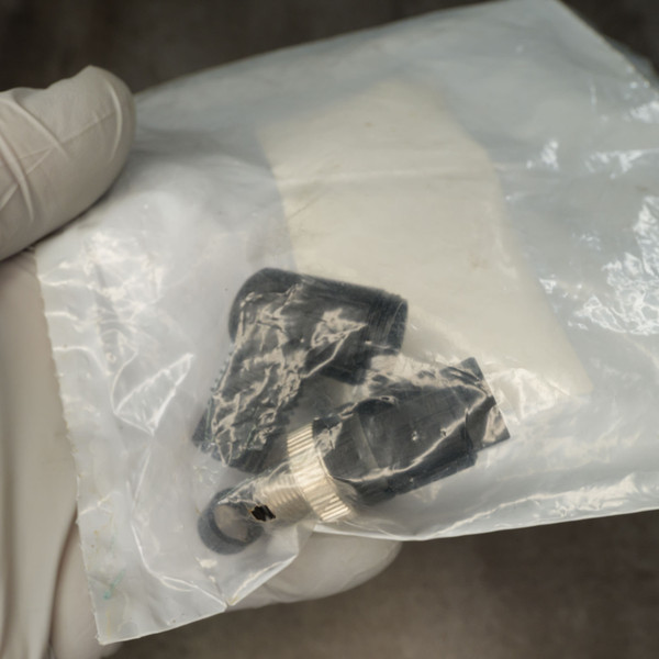 Unused M12 4-pin right-angle connector loose in open poly bag; black body wrapped in protective film, silver knurled coupling ring visible.